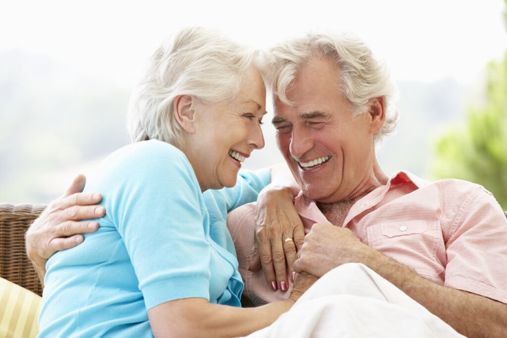 Senior Couple Sitting On Outdoor Seat Together Laughing