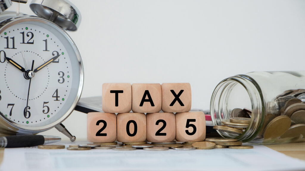 Tax and Vat 2025 Concept. The image shows an alarm clock, a jar of coins, a pen and wooden blocks spelling out TAX 2025. income tax online return form for payment. Expenses, account, VAT, pay tax.
